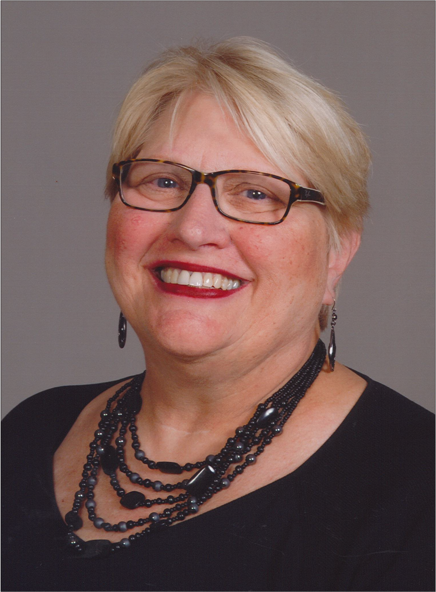 photo of accompanist Joy a white woman with short blond hair and glasses wearing a black shirt and black necklaces